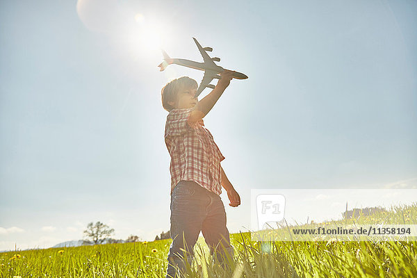 Boy in sunlit field with blue sky playing with toy airplane