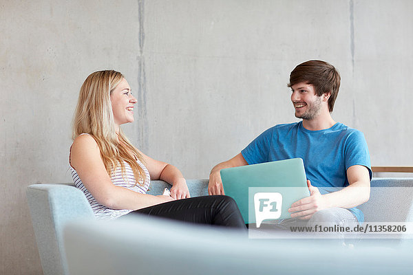 Young male and female students sitting on study space sofa with laptop at higher education college