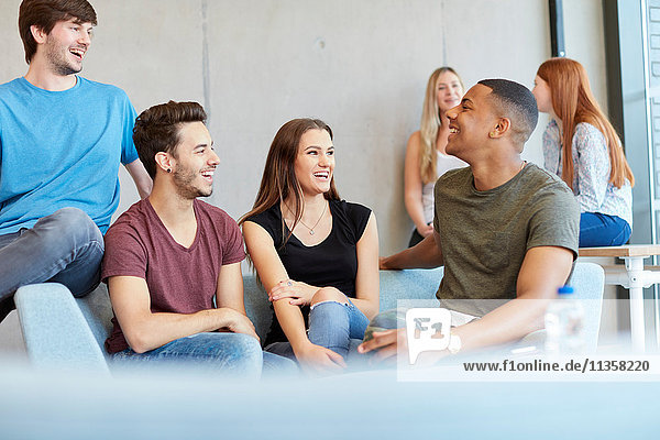 Gruppe junger männlicher und weiblicher Studenten  die auf einem Studienraumsofa sitzen und sich an einer Hochschule unterhalten