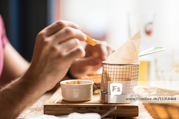 Hand eines jungen Mannes beim Essen von Chips im Restaurant