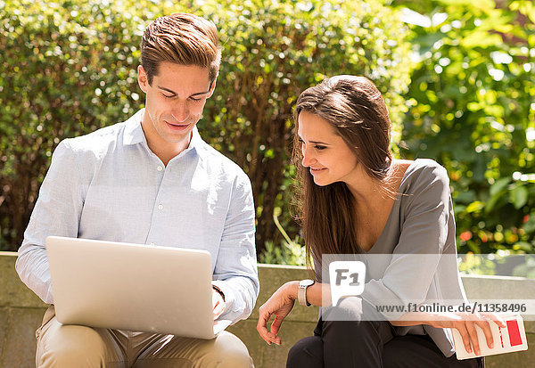 Businessman and woman reading laptop on park bench  London  UK