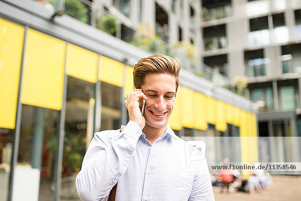 Young businessman talking on smartphone outside office  London  UK