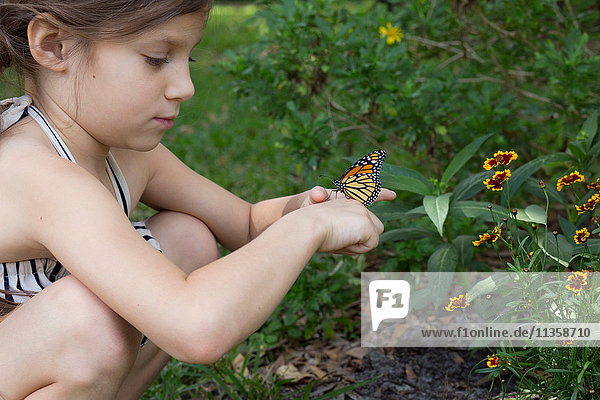 Girl crouching holding monarch butterfly