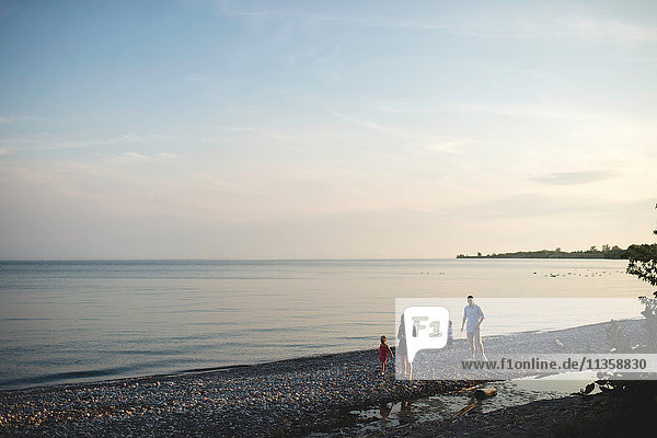 Mittlere erwachsene Eltern spazieren mit Jungen und Mädchen am Kieselsteinstrand des Ontariosees,  Oshawa,  Kanada