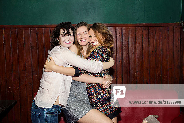 Drei erwachsene Freundinnen bei einer Gruppenumarmung in einer Bar
