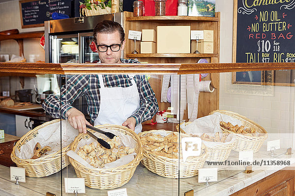 Male worker in bakery  taking fresh goods from basket