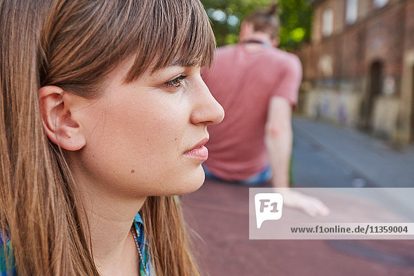 Young couple outdoors  sitting away from each other  sad expression on young woman's face