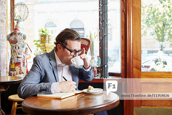 Mann sitzt im Café  trinkt Kaffee  schreibt in ein Notizbuch