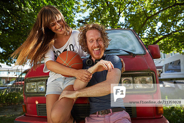 Junges Paar albert im Freien herum  lachend  junge Frau hält Basketball