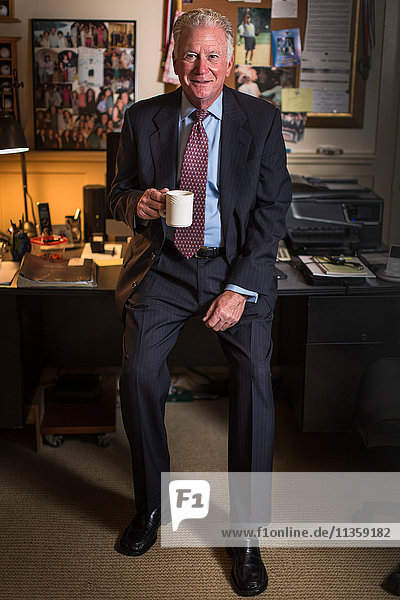 Porträt eines hochrangigen Geschäftsmannes  der auf einem Bürotisch sitzt