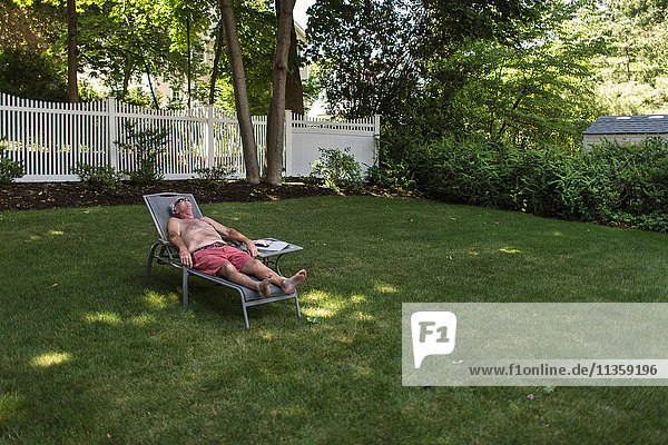 Älterer Mann beim Sonnenbaden im Garten und beim Hören von Kopfhörern