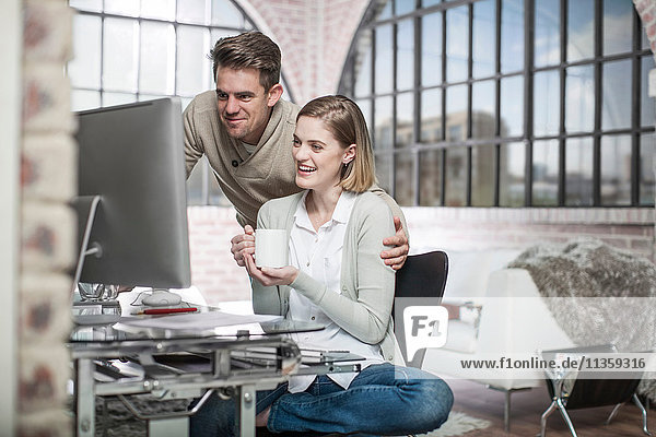 Young woman at home  sitting at desk  looking at computer screen  man beside her  smiling