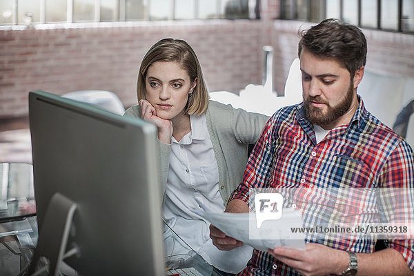 Couple at home  looking at computer screen  man holding paperwork