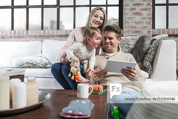 Mutter und Kleinkind sitzen auf dem Sofa  Kleinkind schaut zum digitalen Tablett des Vaters hinüber