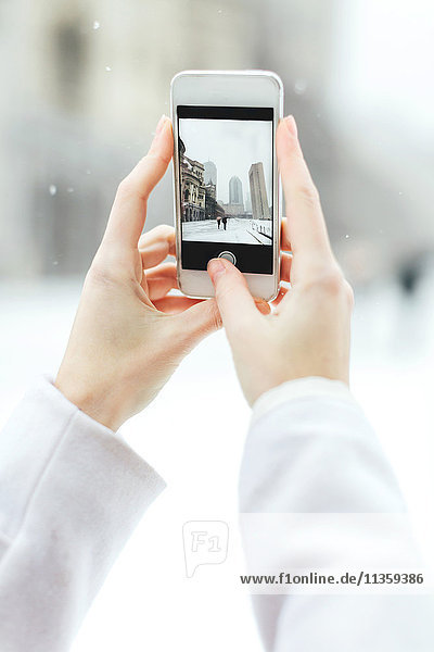 Junge Frau fotografiert mit ihrem Smartphone das Christian Science Centre und das Prudential Building im Schnee Boston Massachusetts USA