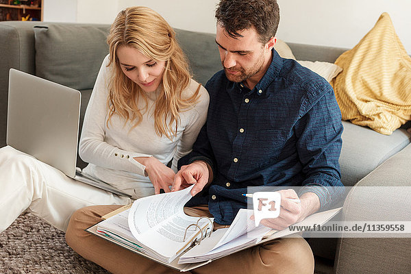 Ehepaar mit Laptop sieht sich Papierkram im Ringordner an