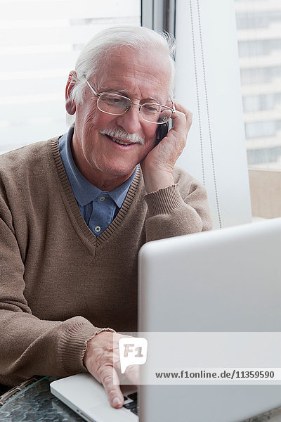 Senior Mann mit Handy und Laptop zu Hause