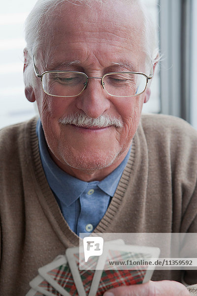 Senior Mann  der zu Hause Karten spielt.