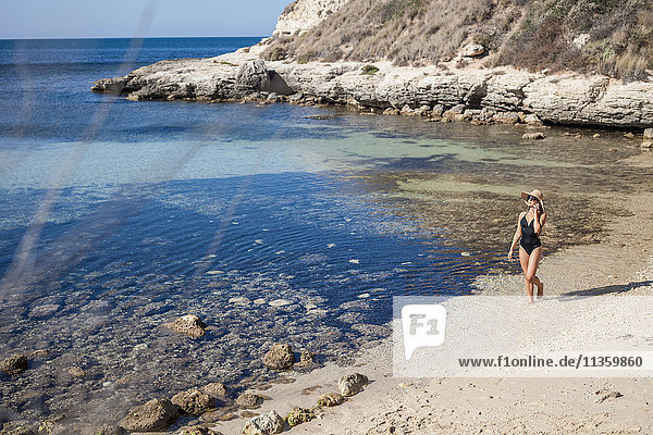 Junge Frau im Badeanzug plaudert am Strand mit einem Smartphone  Villasimius  Sardinien  Italien