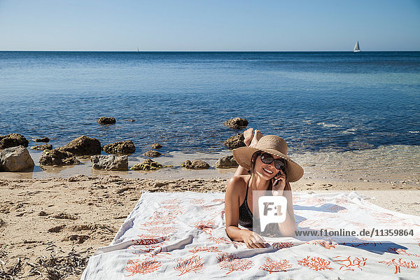 Junge Frau unterhält sich beim Sonnenbaden am Strand mit einem Smartphone  Villasimius  Sardinien  Italien