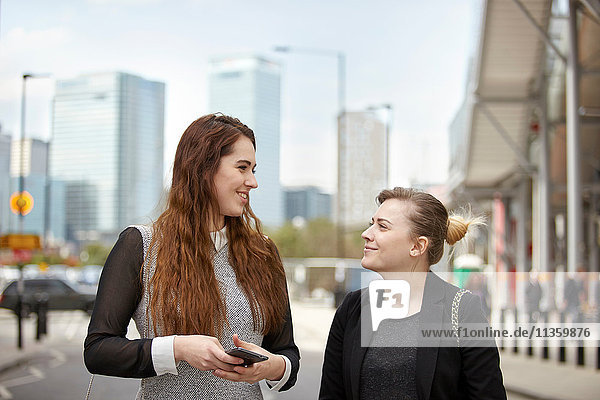 Two young businesswomen talking on city street  London  UK