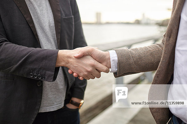 Mid section view of two businessmen shaking hands on waterfront  London  UK
