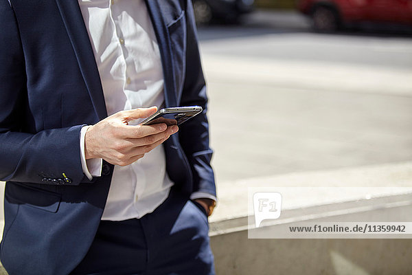 Mid section of businessman texting on smartphone in city
