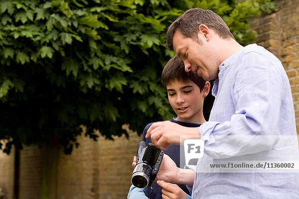Ein erwachsener Mann erklärt seinem Sohn im Garten die Videokamera