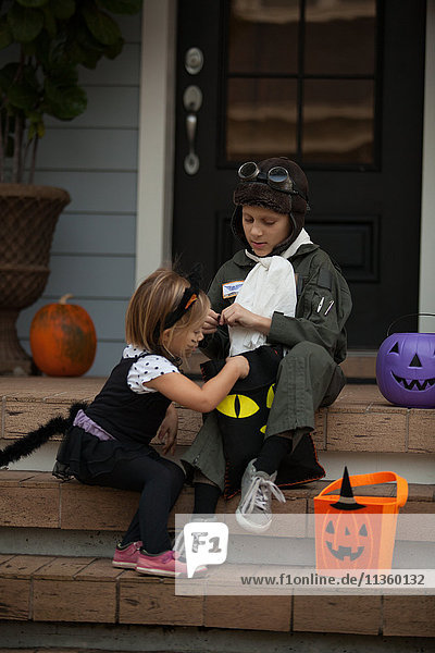 Junge und Schwester Trick oder Behandlung in Katze und Pilot Kostüm sitzen auf der Treppe suchen in Säcken