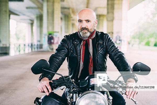 Portrait of mature male motorcyclist sitting on motorcycle under flyover