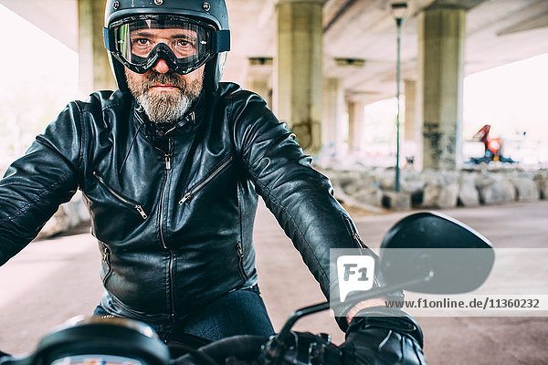 Erwachsener Motorradfahrer mit schwarzem Helm und Schutzbrille auf dem Motorrad unter der Überführung.