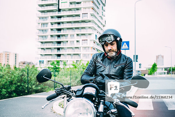 Mature male motorcyclist sitting on motorcycle putting on gloves