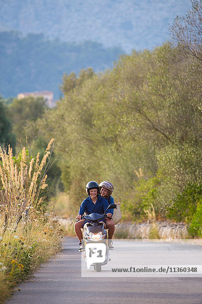 Young couple riding moped on rural road  Majorca  Spain