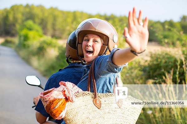 Junge Frau fährt auf der Landstraße auf dem Sozius und winkt  Mallorca  Spanien