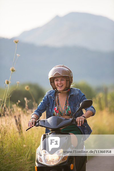 Happy young woman riding moped on rural road  Majorca  Spain