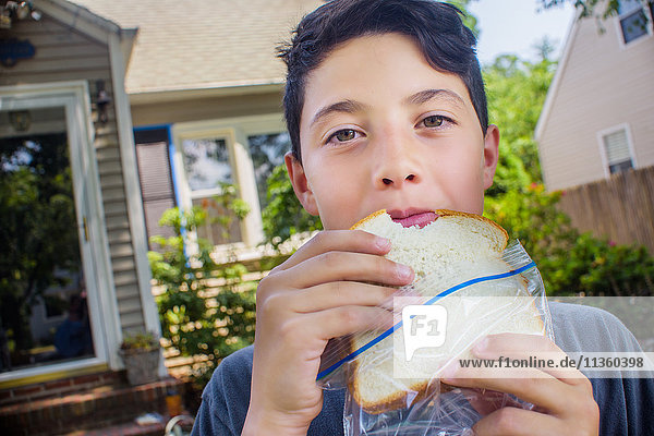 Porträt eines süßen Jungen  der im Garten ein Sandwich isst