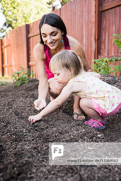 Mutter und junge Tochter pflanzen Samen im Garten
