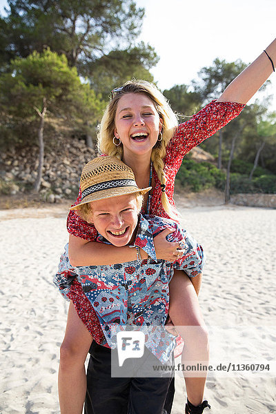 Mann am Strand gibt lächelnder Frau Huckepack  Mallorca  Spanien