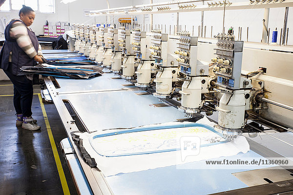 Female factory worker preparing cloth for speed stitching programmed embroidery machine in clothing factory