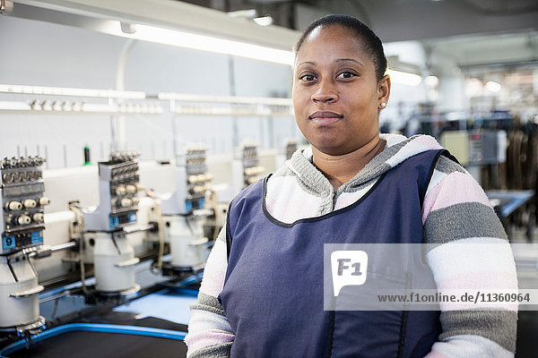 Portrait of female factory worker in front of programmed embroidery machines in clothing factory