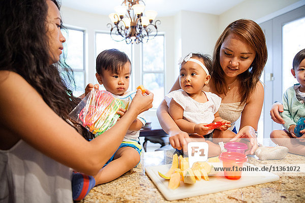 Women feeding baby son and daughter fruit on kitchen counter