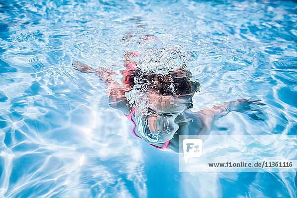 Mädchen schwimmt unter Wasser im sonnenbeschienenen Schwimmbad