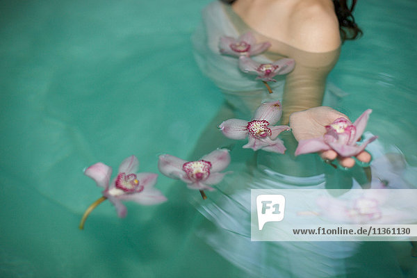 Schnappschuss einer jungen Frau im Schwimmbad eines Heilbades mit schwimmenden violetten Orchideen