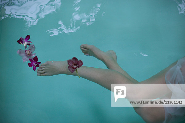 Nackte Beine und Füße einer Frau  die mit Orchideen unter Wasser im Whirlpool schwimmt
