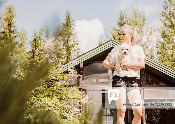 Frau im Garten mit einem Hund  der einen Coton de Tulear trägt  Orivesi  Finnland