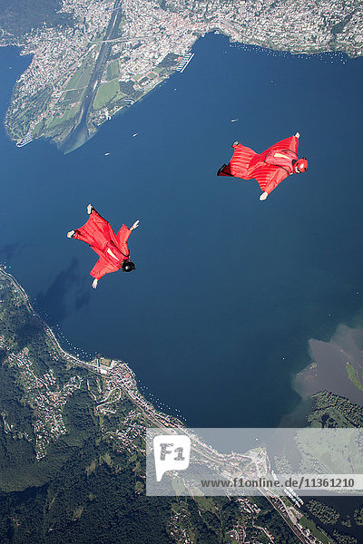 Zwei Fallschirmspringerpiloten in Wingsuit trainieren und fliegen eng beieinander über dem See  Locarno  Tessin  Schweiz