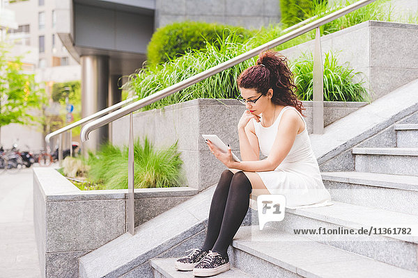 Woman sitting on steps using digital tablet  Milan  Italy