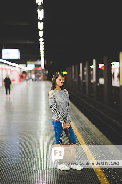 Young woman waiting on edge of railway platform at night