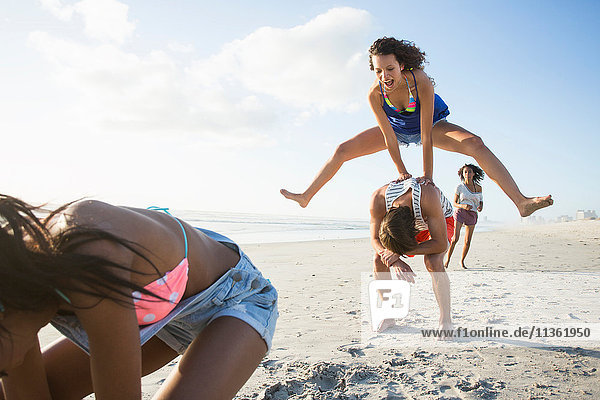 Young man and three female friends playing leapfrog on beach  Cape Town  South Africa
