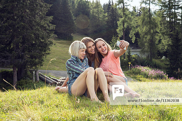 Drei erwachsene Freundinnen sitzen für Smartphone-Selfie im Feld  Sattelbergalm  Tirol  Österreich